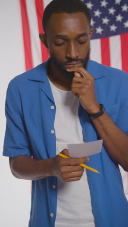 Vertical-Video-Shot-Of-Man-Next-To-Booth-With-Ballot-Paper-In-American-Election-Deciding-How-To-Cast-His-Vote-1